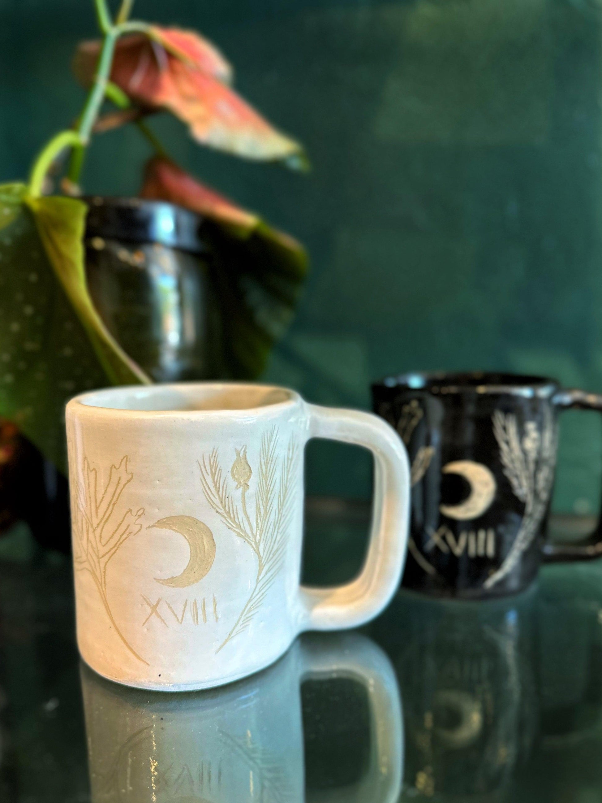 Two mugs with decorative designs on a reflective surface
