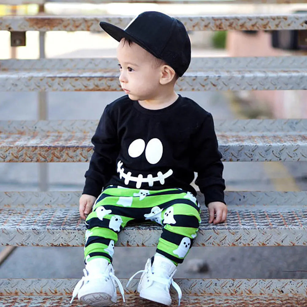 Child wearing a black shirt with a skeleton design and green striped pants with ghost patterns, sitting on metal steps.