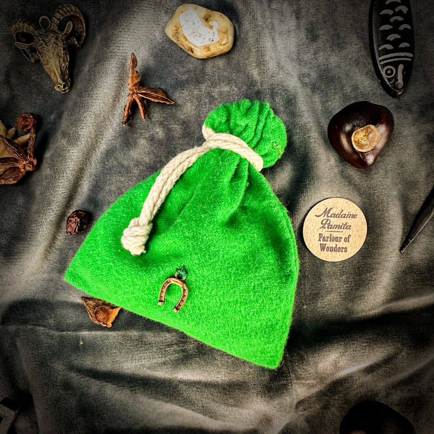 Green drawstring bag with a horse shoe charm on a textured surface with decorative items.