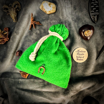 Green drawstring bag with a horse shoe charm on a textured surface with decorative items.