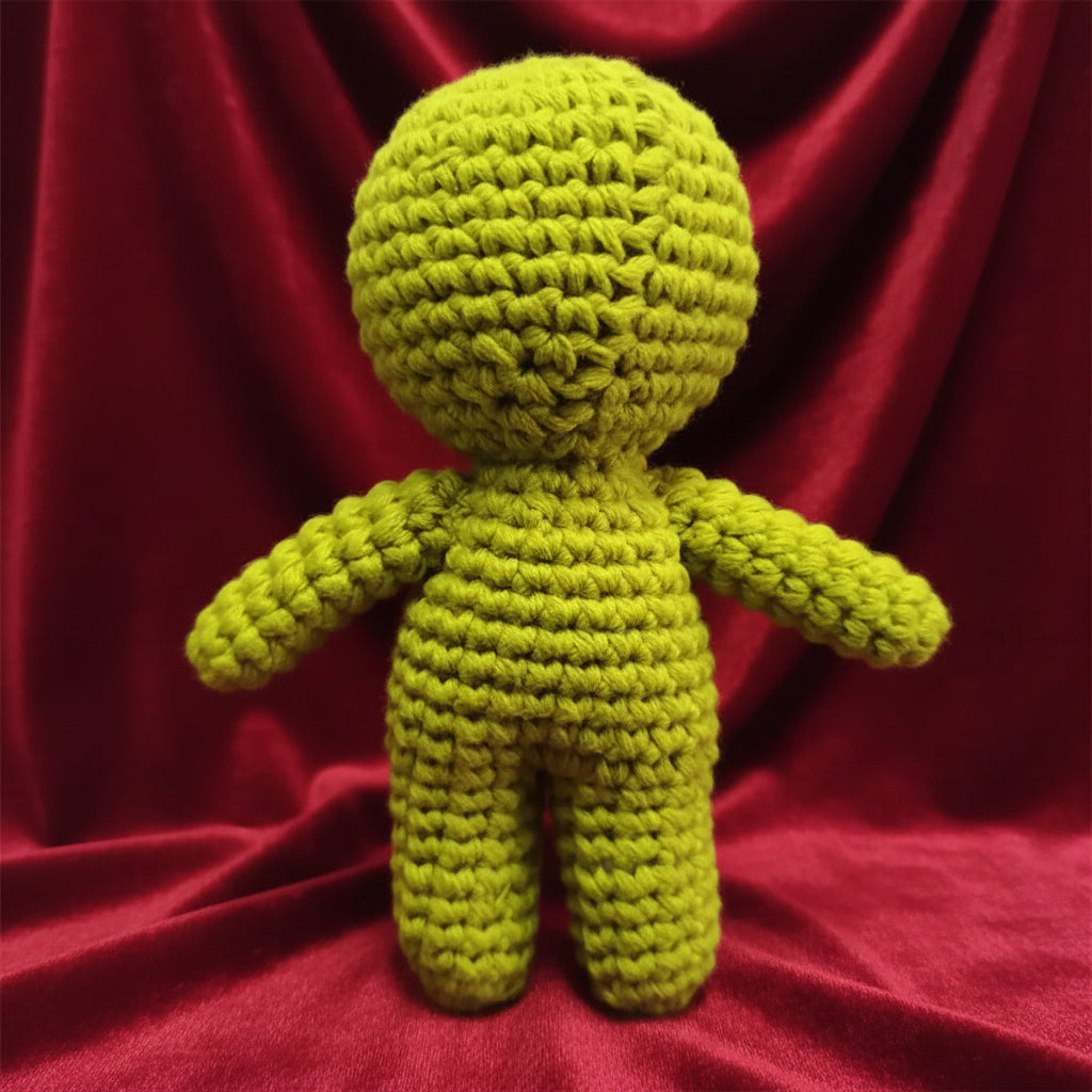 A bright lime green crocheted doll with a round head, simple arms, and legs, standing upright on a light gray surface.