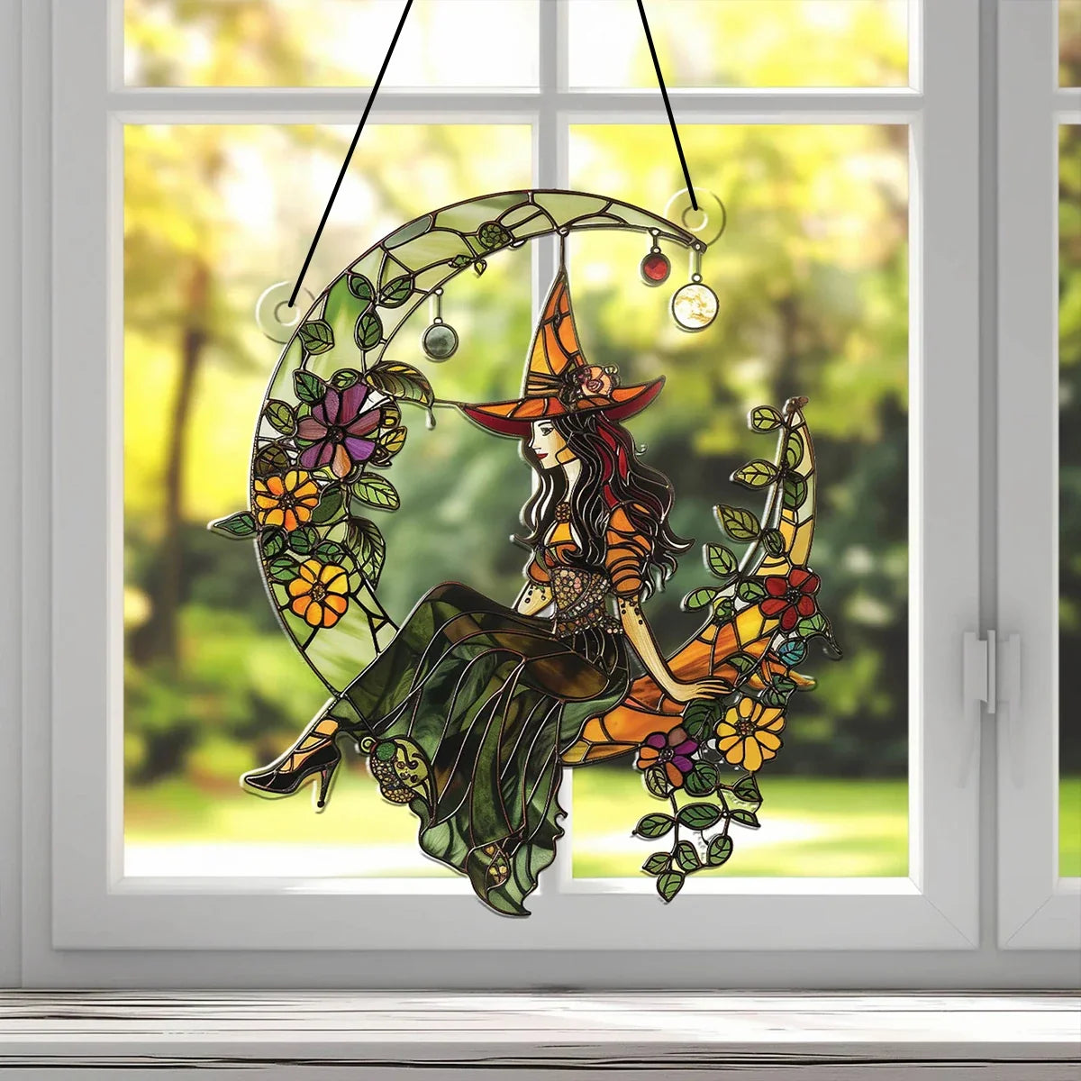 Decorative stained glass panel of a witch on a crescent moon with flowers, hanging in front of a window.