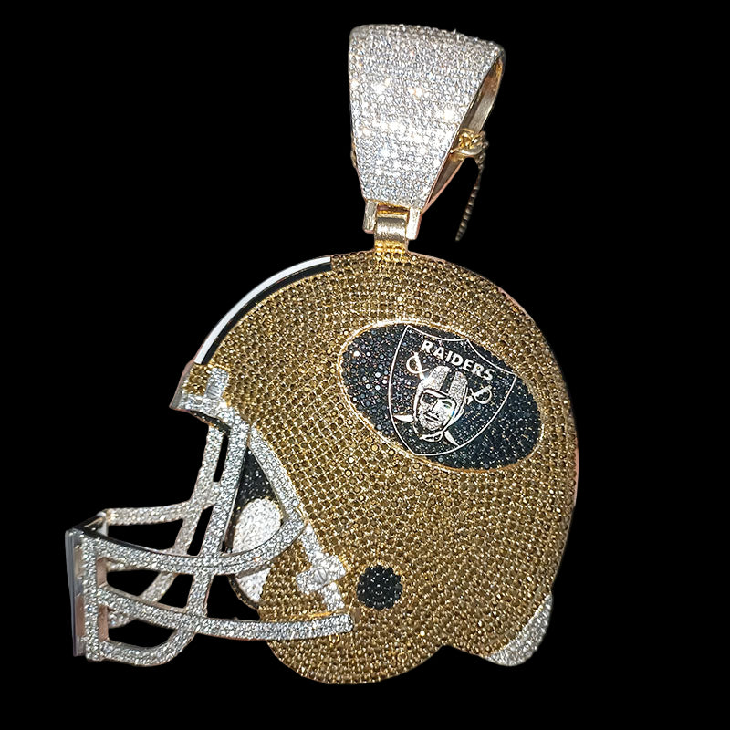 Gold and silver helmet-shaped pendant with Raiders logo held in a hand against a dark background