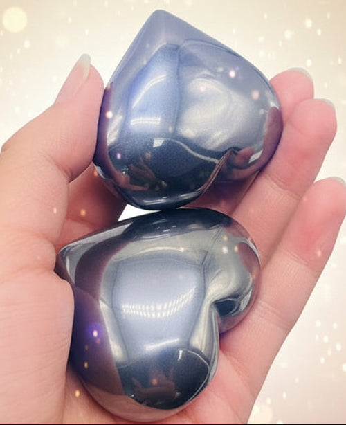 Hand holding three shiny, metallic-looking stones against a green grass background