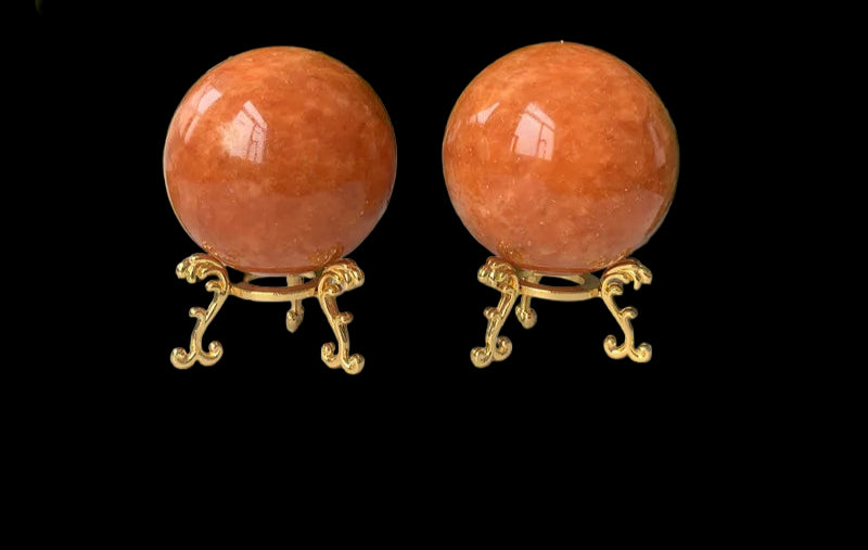 Two orange spherical objects on gold stands with green plants in the background