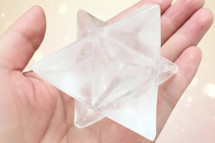 Clear star-shaped crystal held in a hand with a green plant background