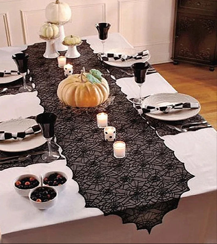 Halloween-themed table setting with black lace tablecloth, pumpkins, and checkered napkins.