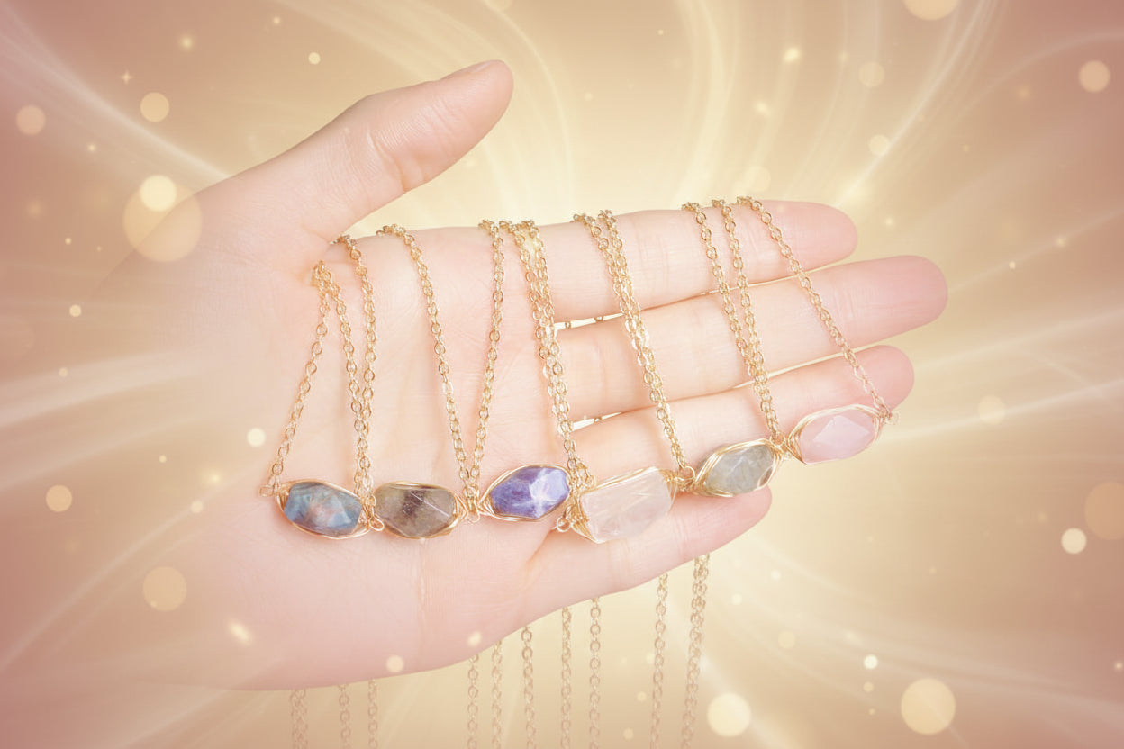 Hand holding multiple gold necklaces with stone pendants against a beige background