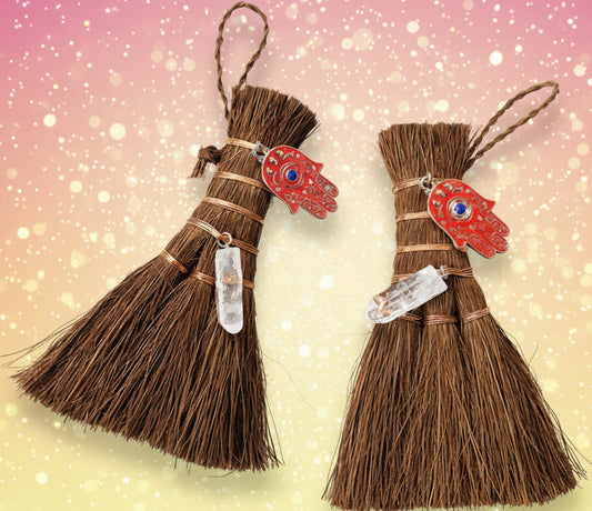 Two small broom ornaments with red fish-shaped charms on a light background