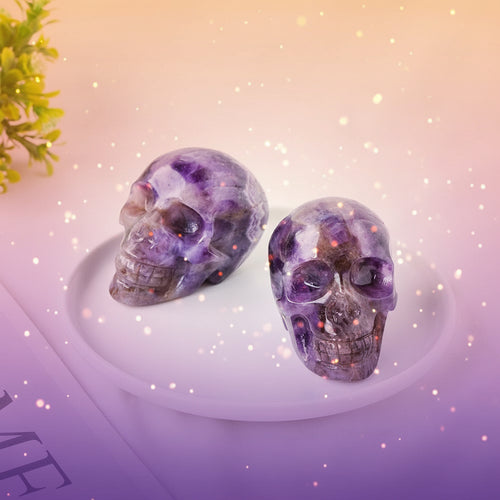 Two purple crystal skulls on a white plate with a green plant in the corner.