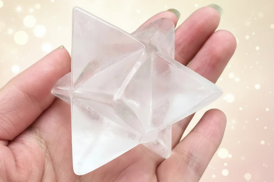 Clear crystal pyramid held in a hand with a green plant background
