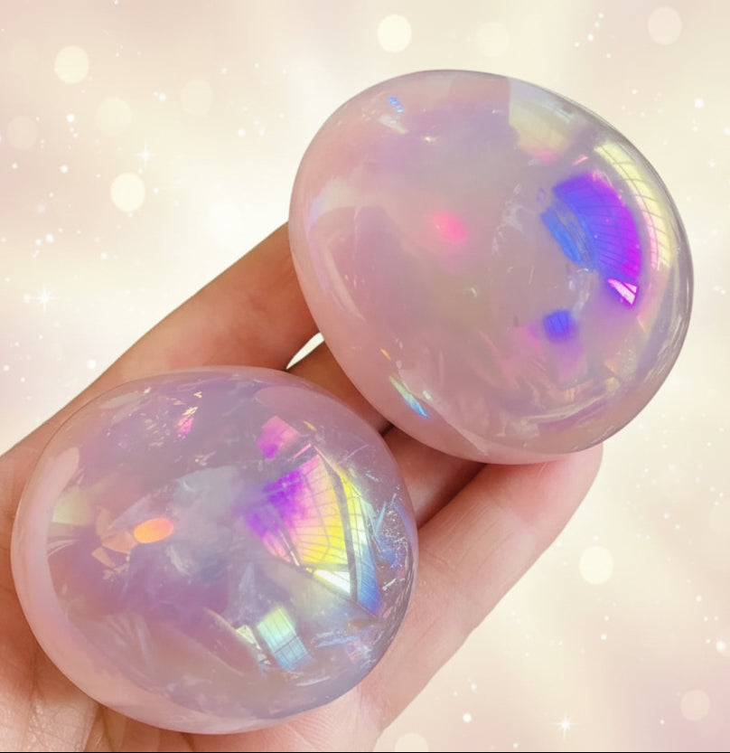 Two iridescent gemstones held in a hand with a green leafy background