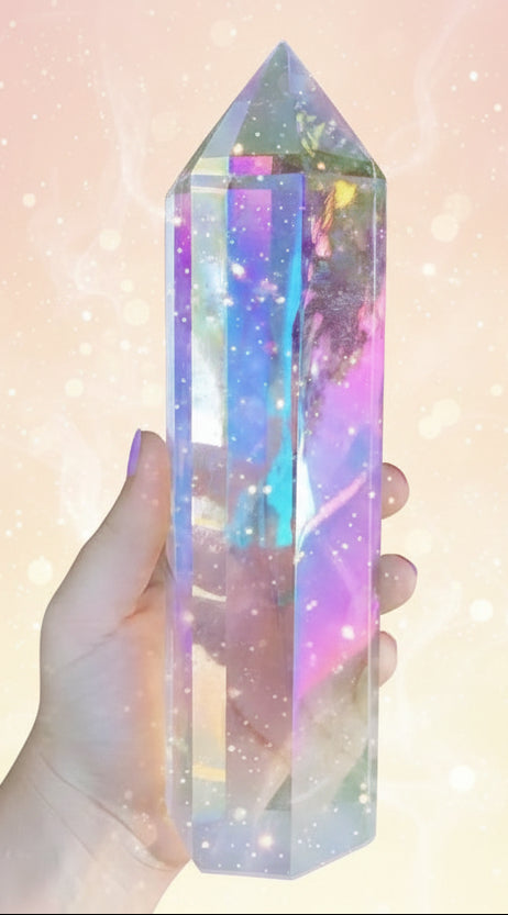 Hand holding a colorful crystal prism in front of green foliage