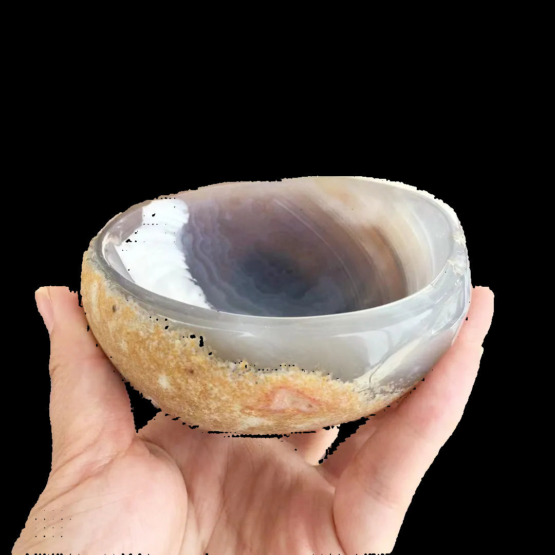 Hand holding a polished stone bowl with a pattern of concentric circles against a background of similar stone bowls.