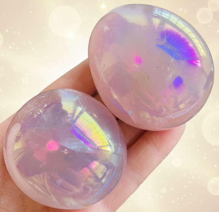 Two iridescent gemstones held in a hand with a green leafy background