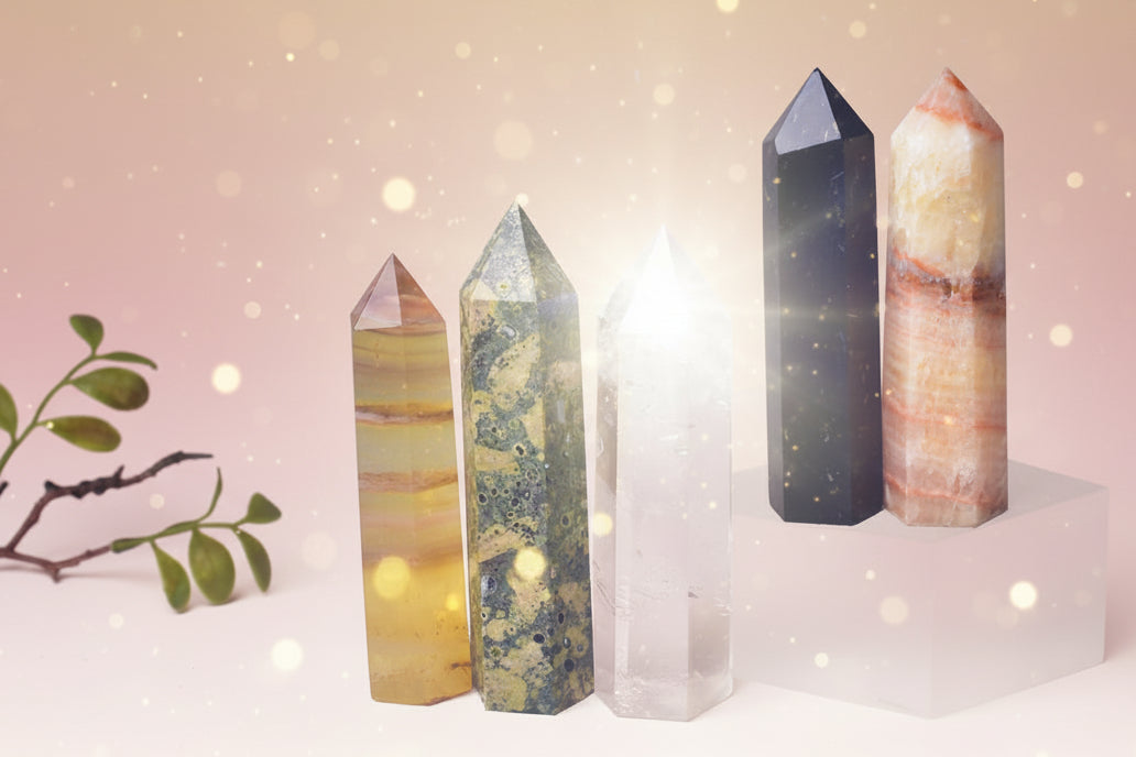 Five crystal towers of different colors and patterns on a textured surface with a plant in the background.