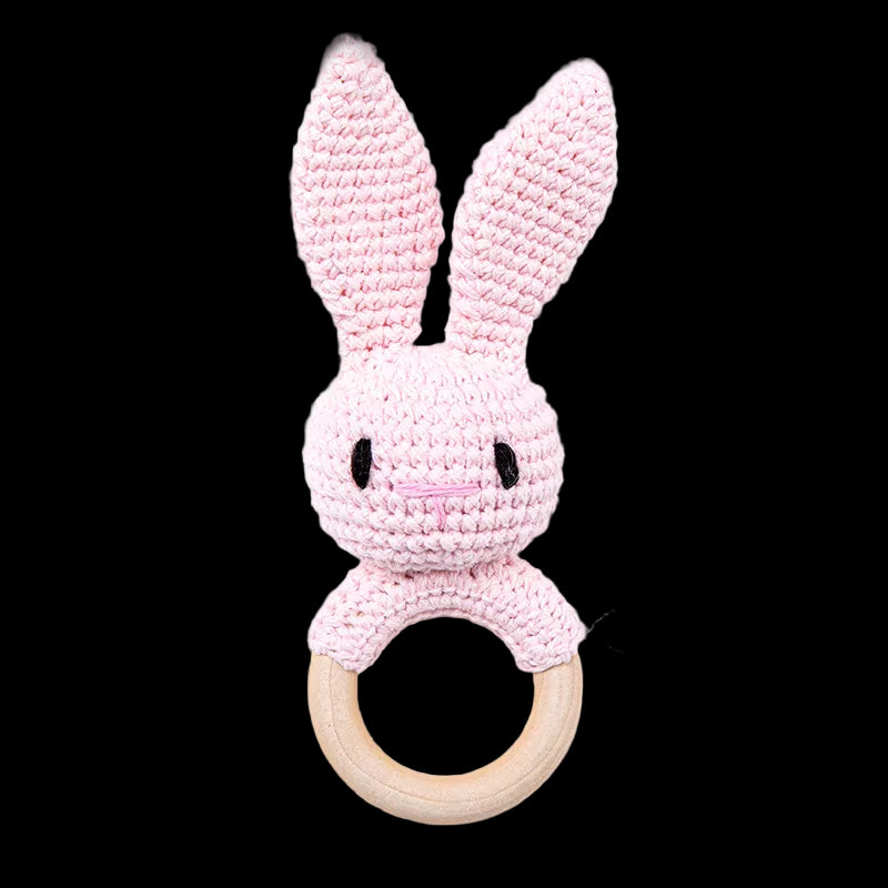 Pink crocheted bunny rattle with wooden ring on a white background