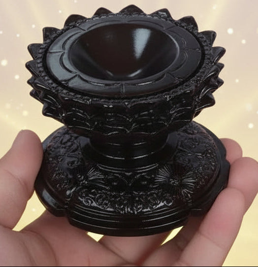 Hand holding a dark wooden object with intricate carvings on a light background