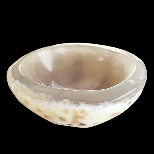 Hand holding a small, round, beige stone with a blurred background of similar stones.