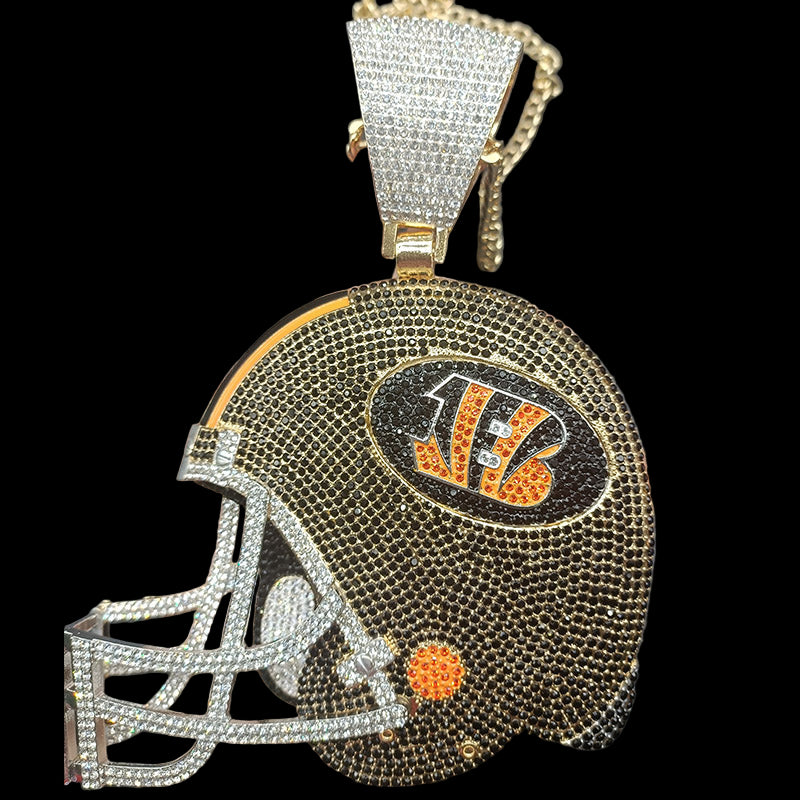 Decorative helmet pendant with rhinestones and a chain, held by a hand against a dark background.