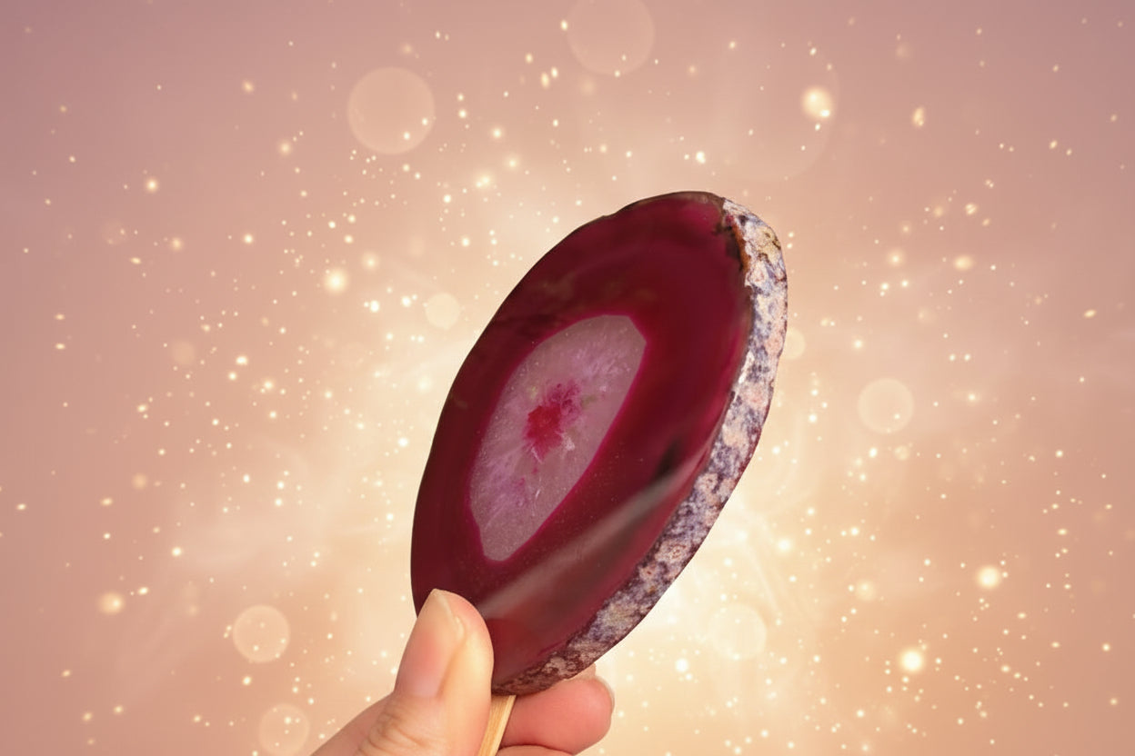 Hand holding a purple agate stone with green foliage in the background