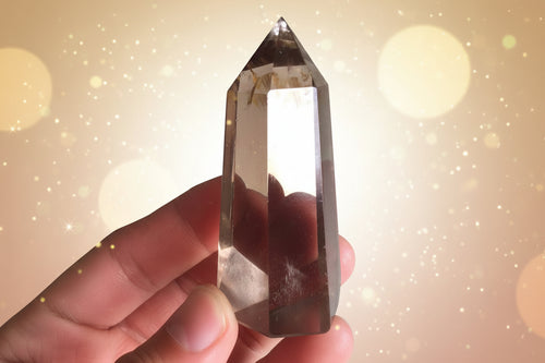 Clear crystal held in a hand with a blurred green plant and white surface in the background