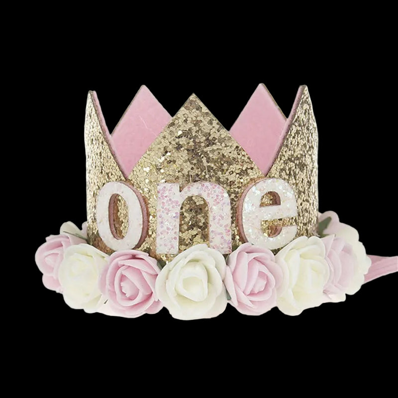 Gold and pink tiara with 'one' and floral decorations on a white background