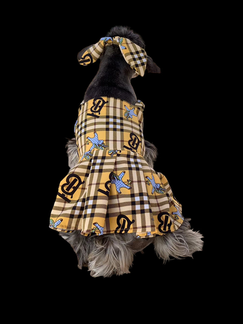 Dog wearing a plaid dress with a checkered headband on a wooden deck.