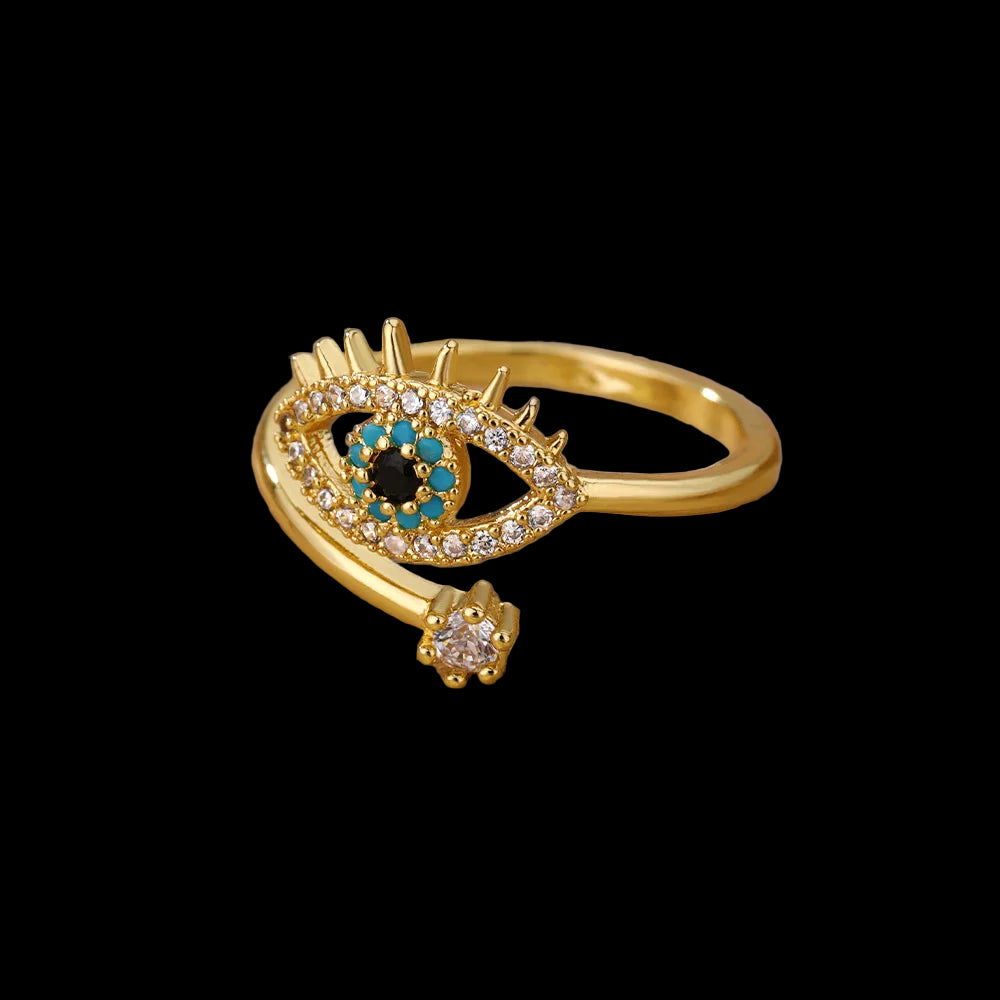 Gold ring with eye design and gemstones on a beige surface
