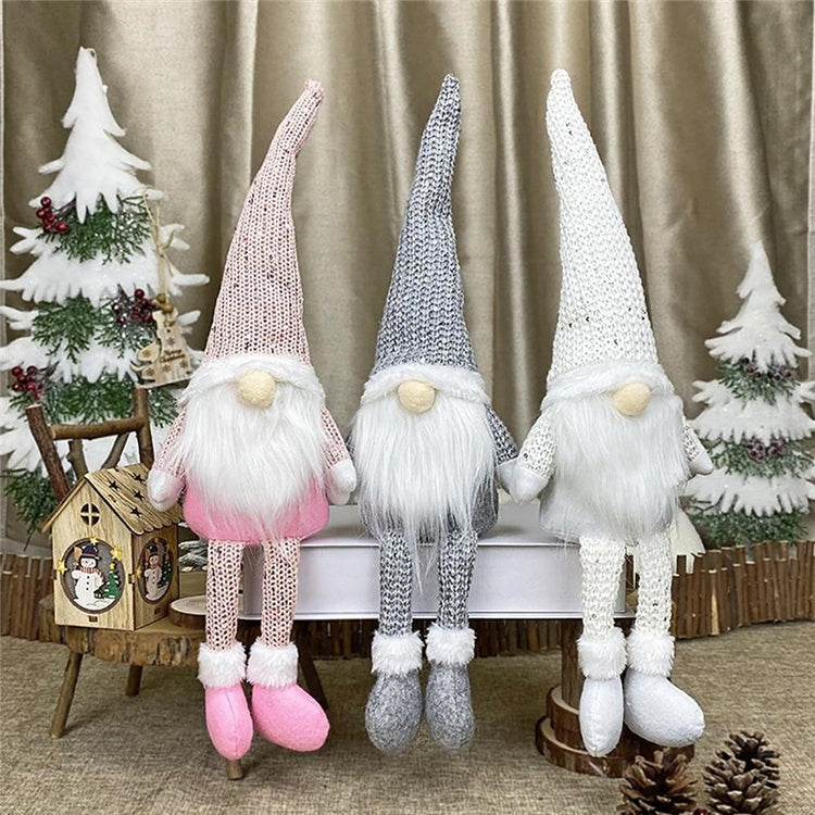 Three knitted gnomes with long beards in pink, gray, and white standing in front of a Christmas-themed background.