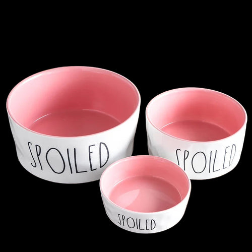Three pet bowls with pink interiors and 'SPOILED' text on a wooden surface, with 'Good Housekeeping' branding.