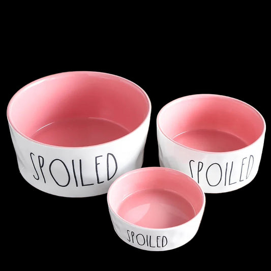 Three pet bowls with pink interiors and 'SPOILED' text on a wooden surface, with 'Good Housekeeping' branding.