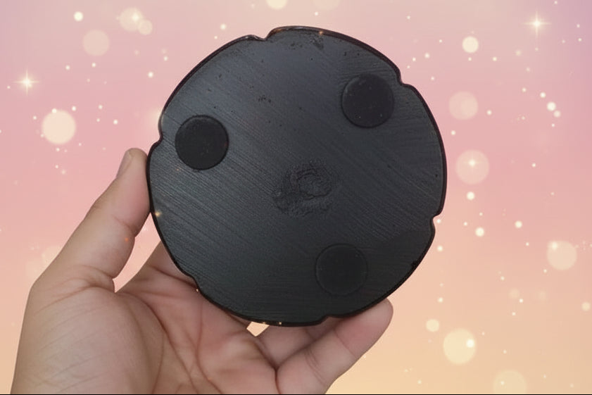 Black circular object with textured surface held by a hand on a white background