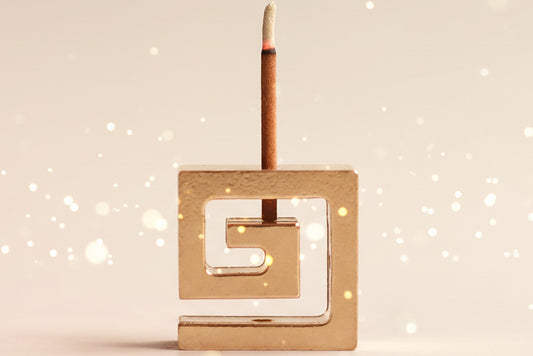 Brass incense holder with a single incense stick on a gray background