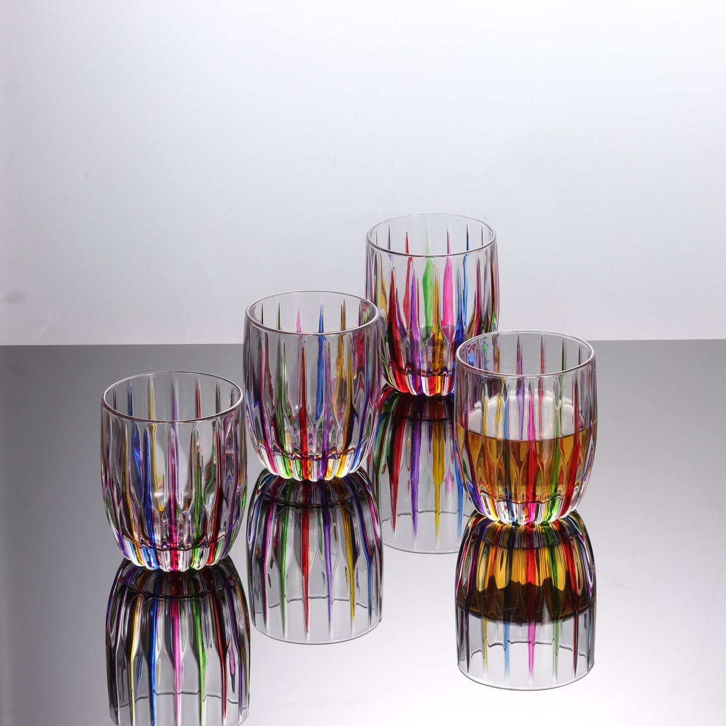 Set of colorful glass tumblers on a reflective surface with a white background
