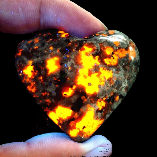 Heart-shaped rock with fiery orange and red patterns held between fingers against a green leafy background