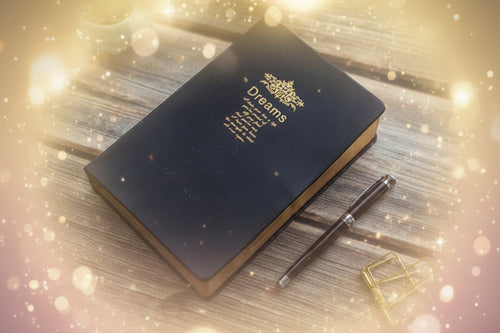 Black notebook with gold embossed text on a wooden surface with a pen and small plant.