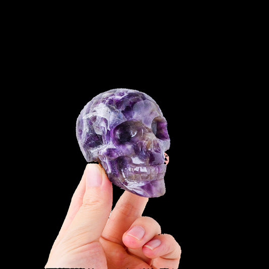 Hand holding a purple crystal skull against a light gray background