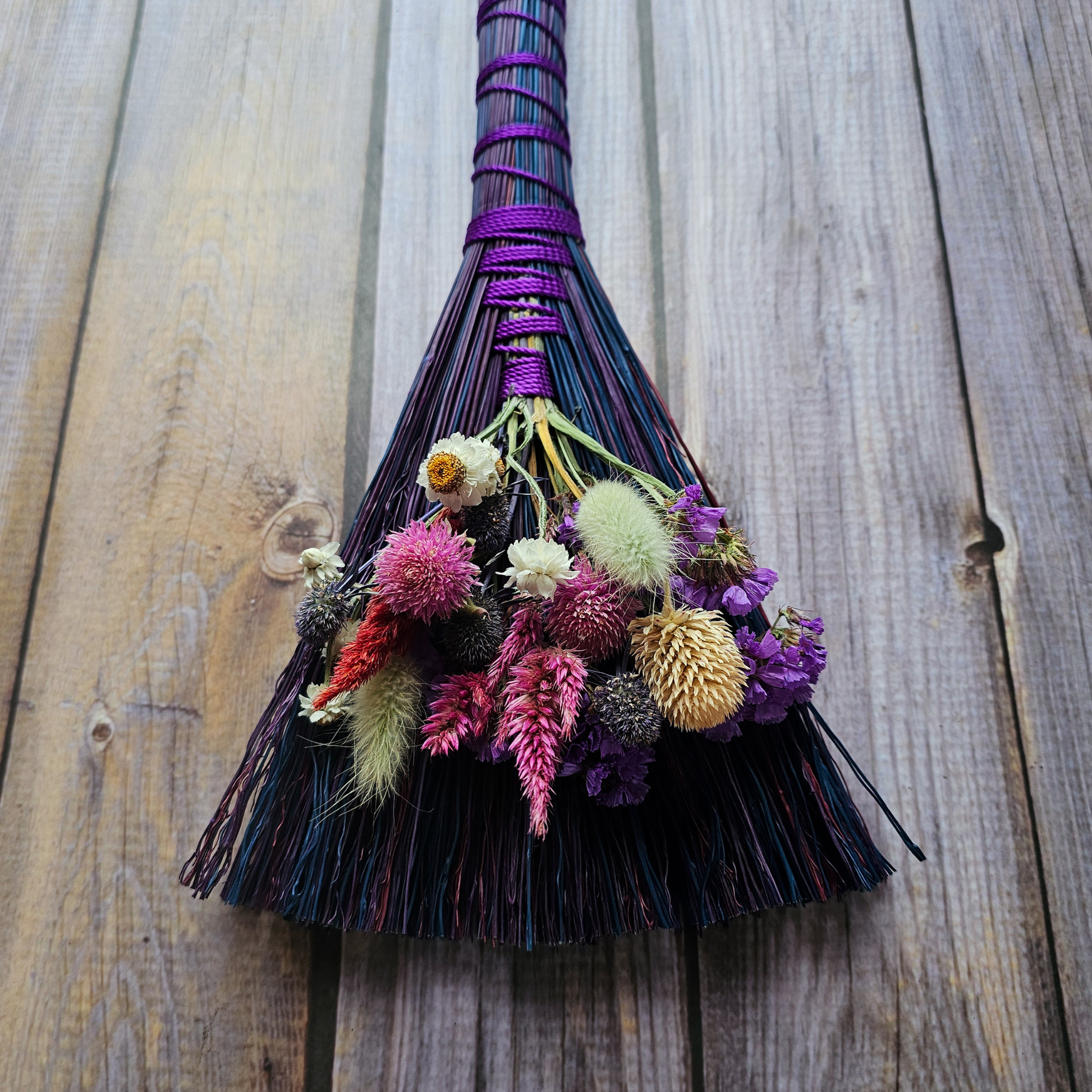 Decorative broom with colorful flowers on a wooden surface