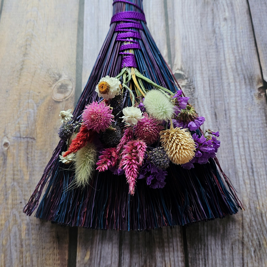 Decorative broom with colorful flowers against a wooden background