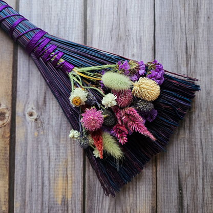 Decorative broom with colorful flowers on a wooden background