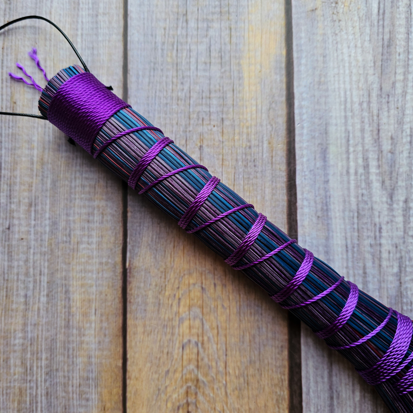 Purple and black striped whip on a wooden surface