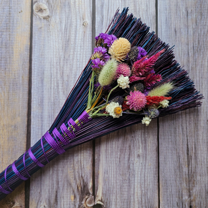 Decorative broom with colorful flowers on a wooden background