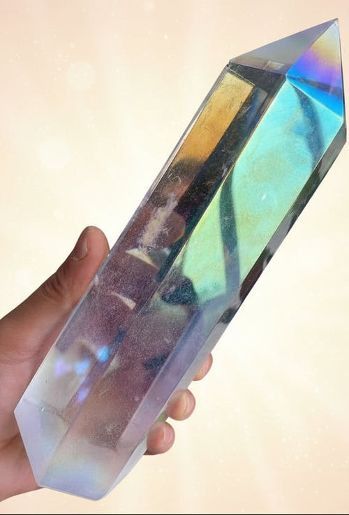 Iridescent crystal prism held by a hand with a plant in the background