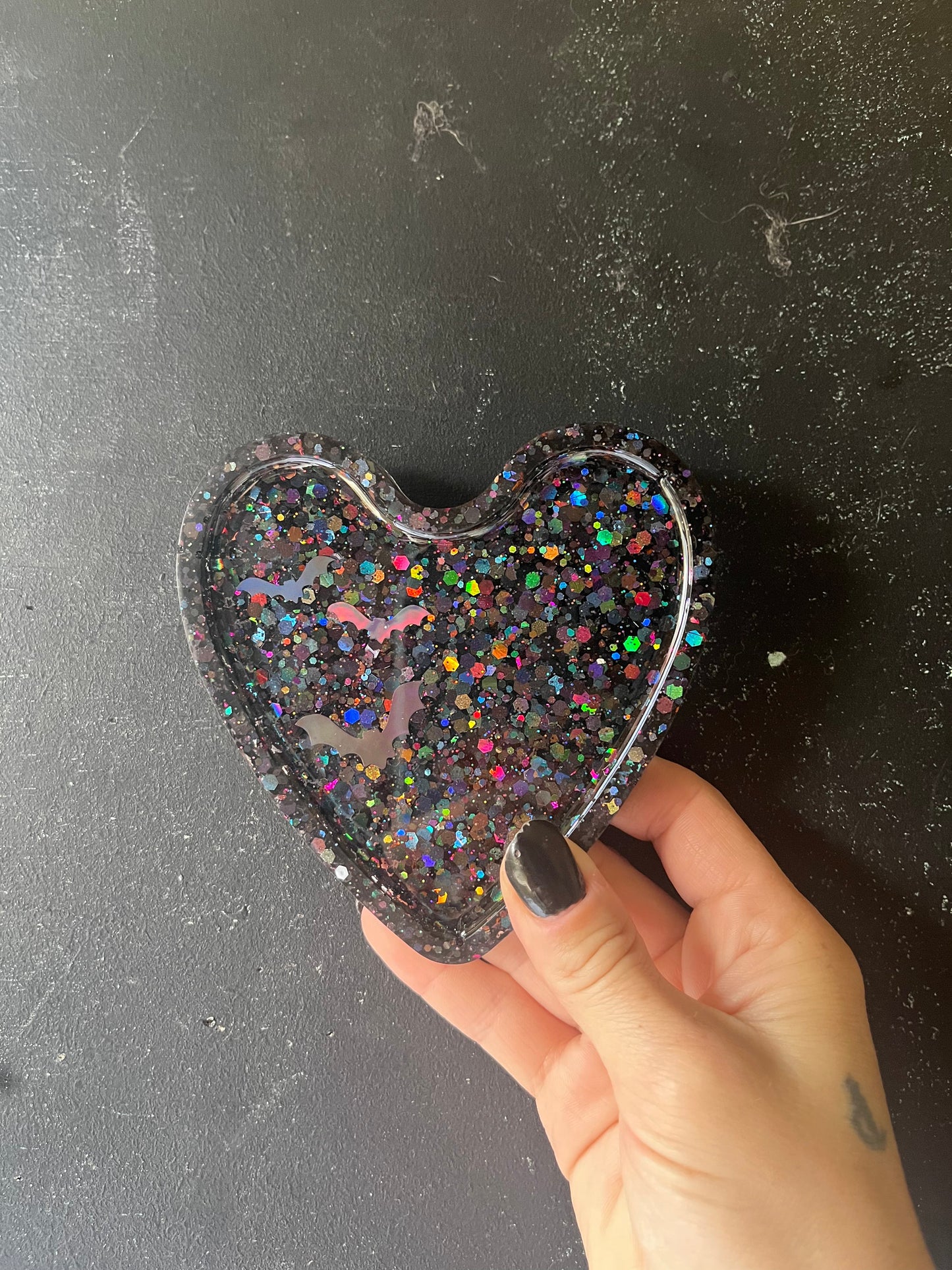 Heart-shaped object with glitter held by a hand on a dark surface