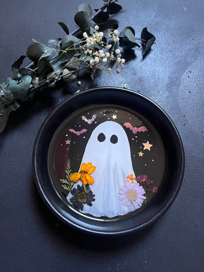Decorative plate with a ghost design surrounded by flowers on a dark surface.