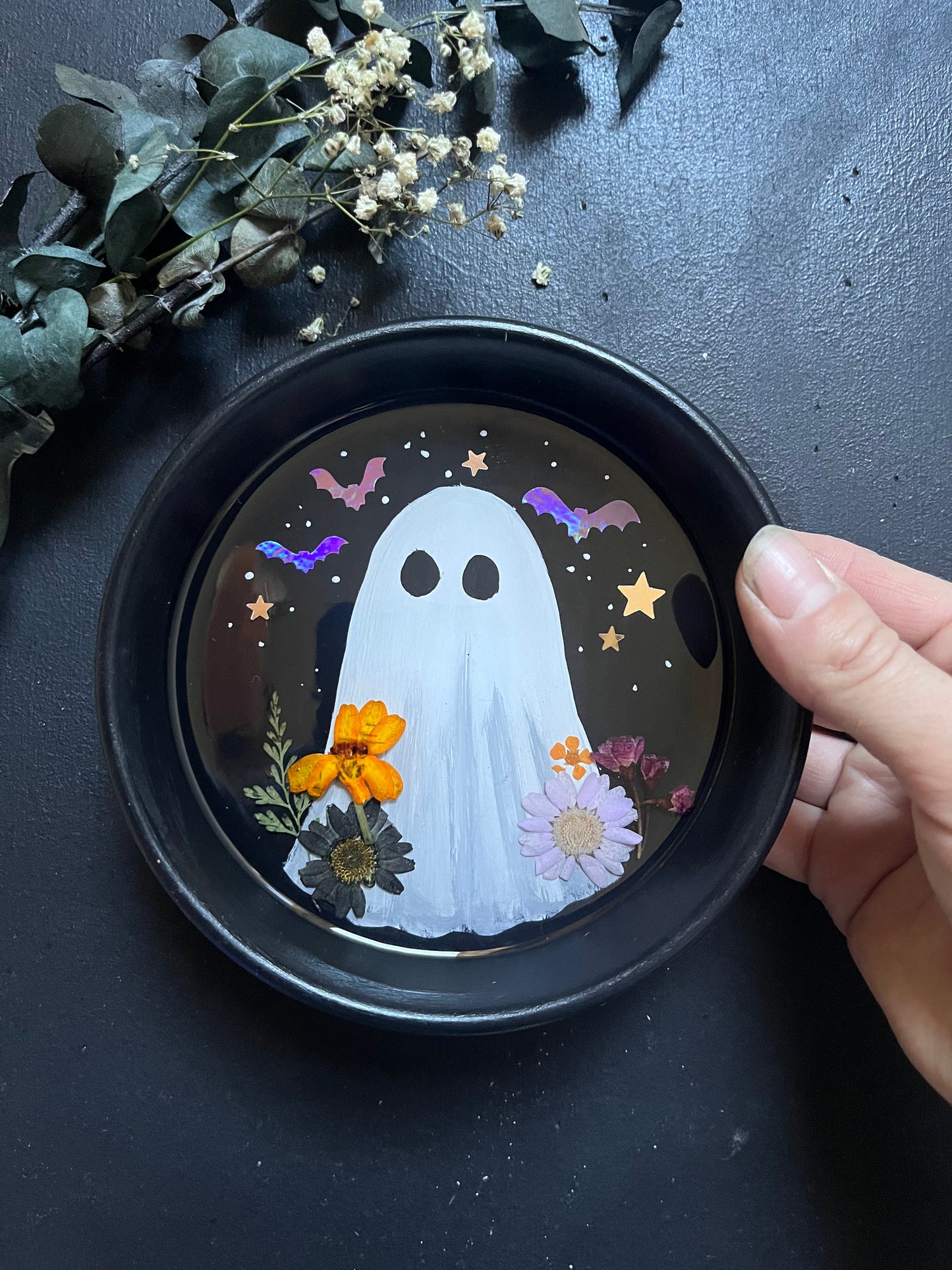 Decorative coaster with a ghost design held by a hand on a dark surface.