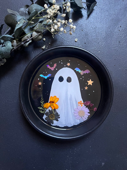 Decorative plate with a ghost design on a dark surface with flowers.