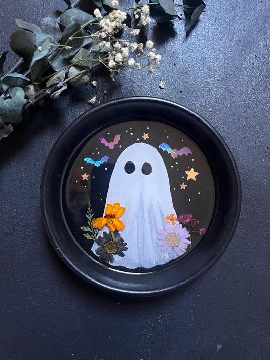 Decorative plate with a ghost design on a dark surface with flowers.