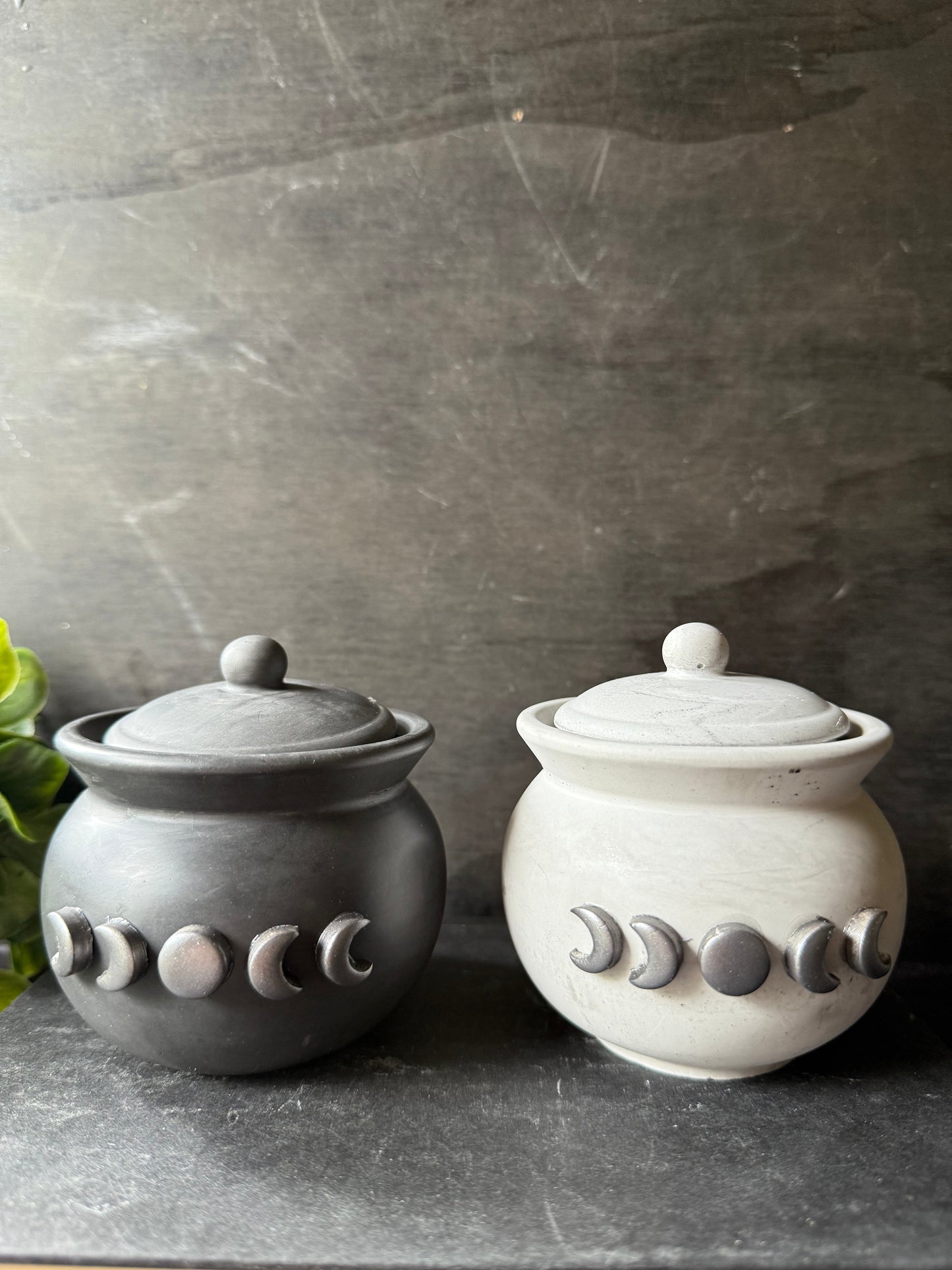Two ceramic jars with lid designs resembling moon phases on a gray surface.